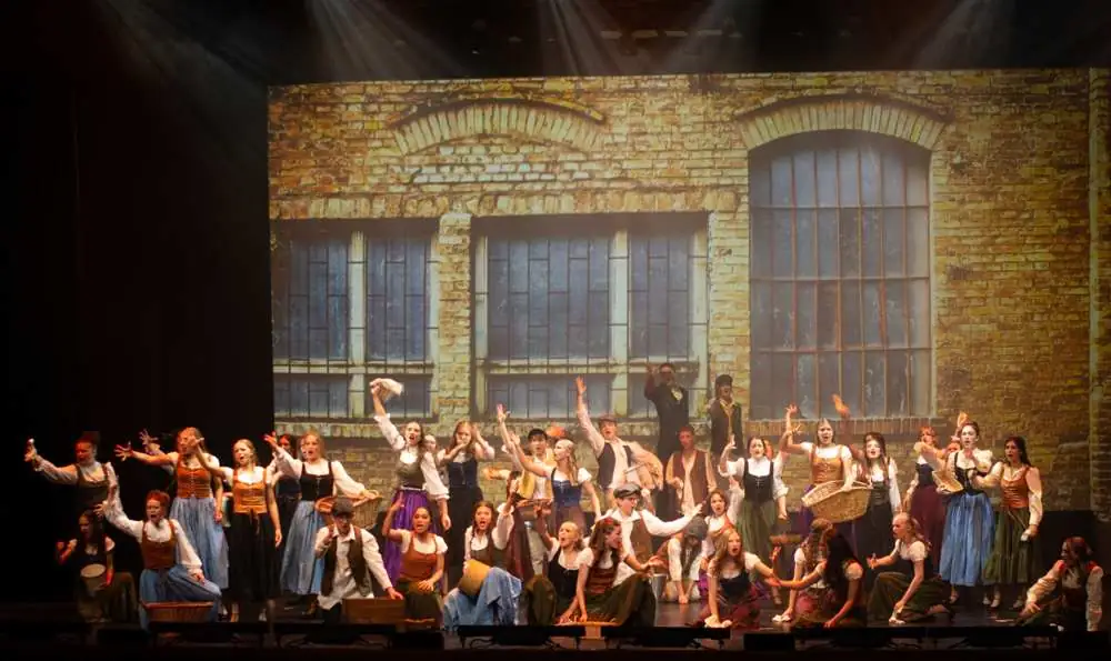 A huge senior company singing in front of a brick factory wall