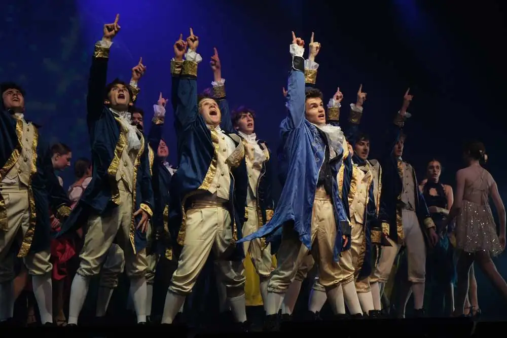 Senior performers in blue and gold coats pointing skyward