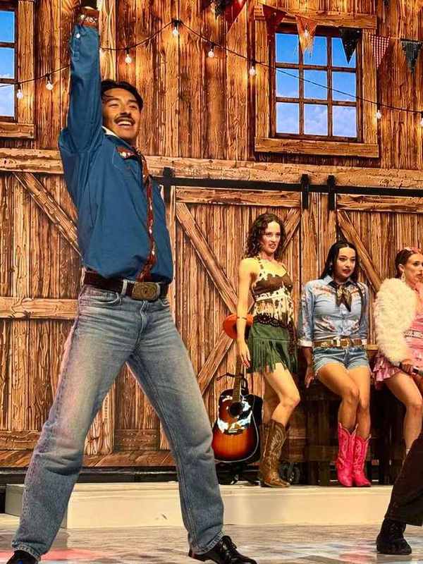 A performer with an arm raised in front of the barn set