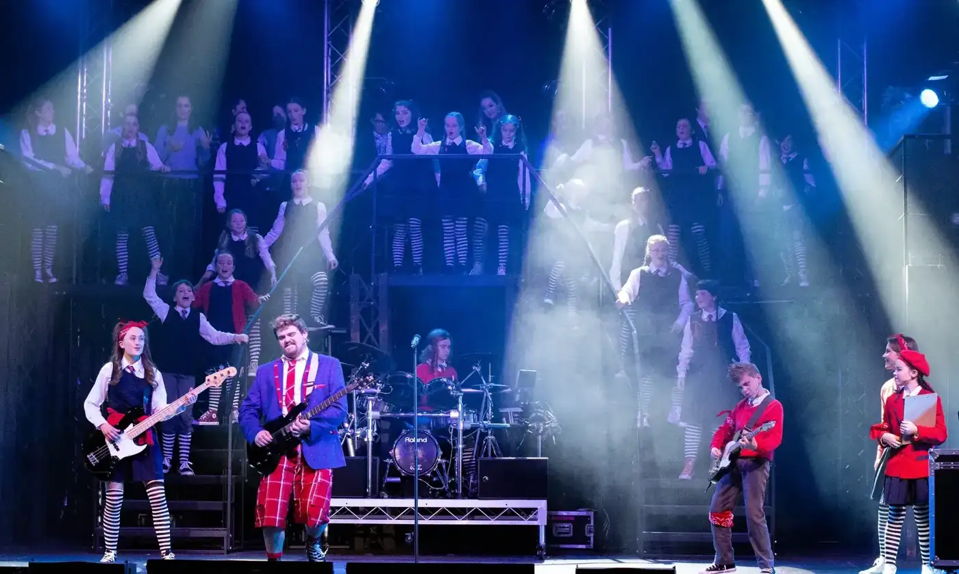 A Pelican band and cast on stage under bright blue and white spotlights
